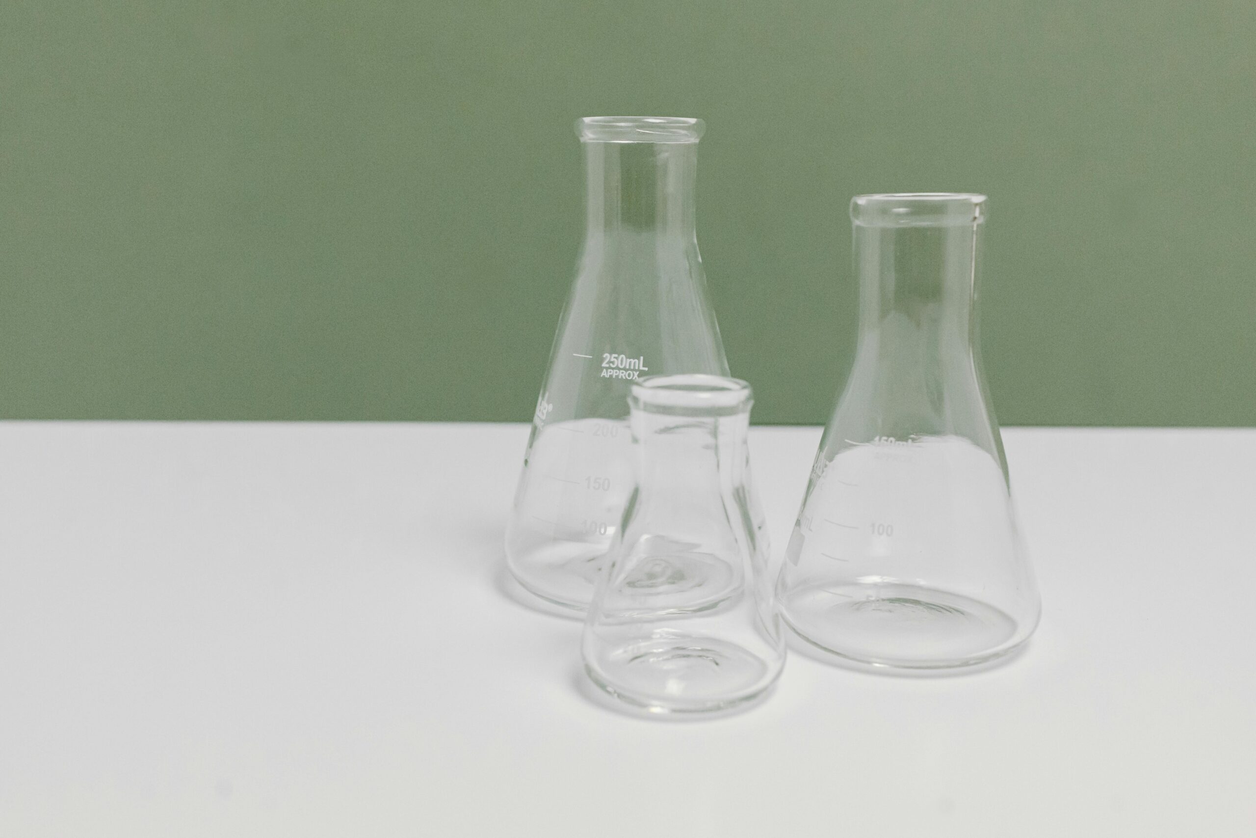 A set of three clear glass laboratory flasks on a clean white and green background, ideal for science themes.